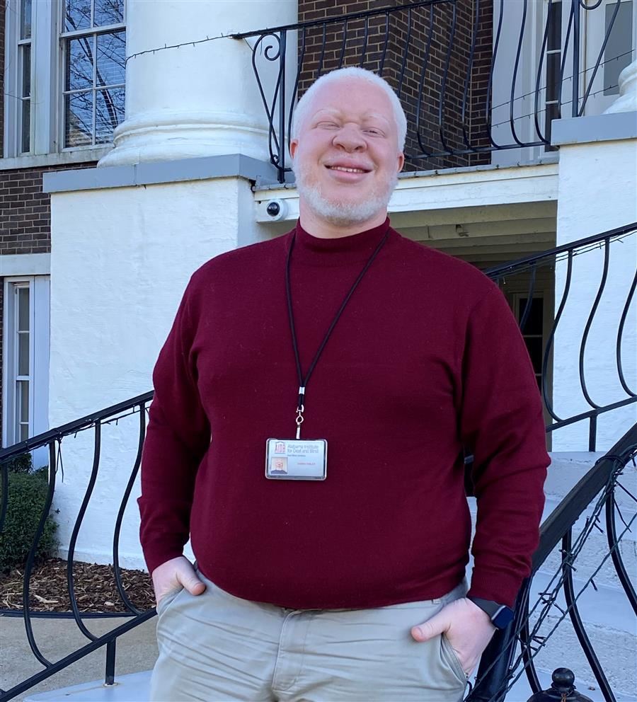 DannyRay Finley smiles to camera while wearing a red sweater and khaki pants.